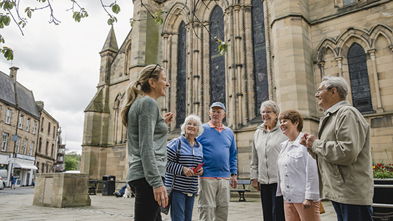 Image shows group of mature adults on a guided vacation abroad. They are walking around the city with a guide learning about the local culture and history of their destination.