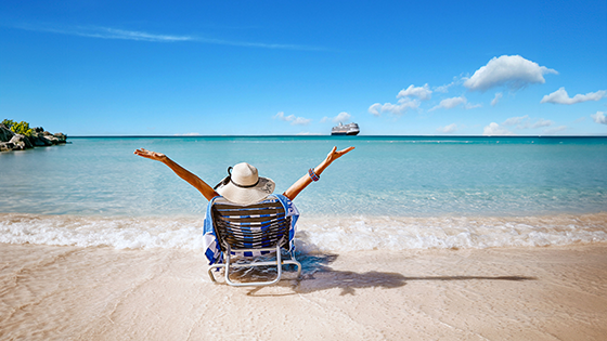 Woman sitting in a beach chair on the sand looking off into the water with her hands in the air. 