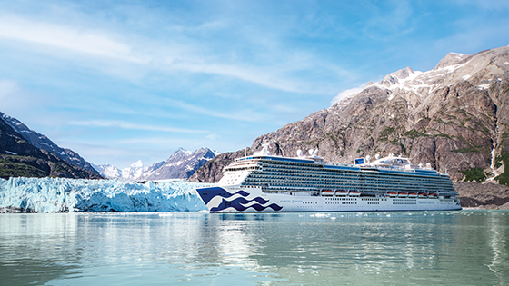Daytime view of cruise ship along the coast with mountain in background.